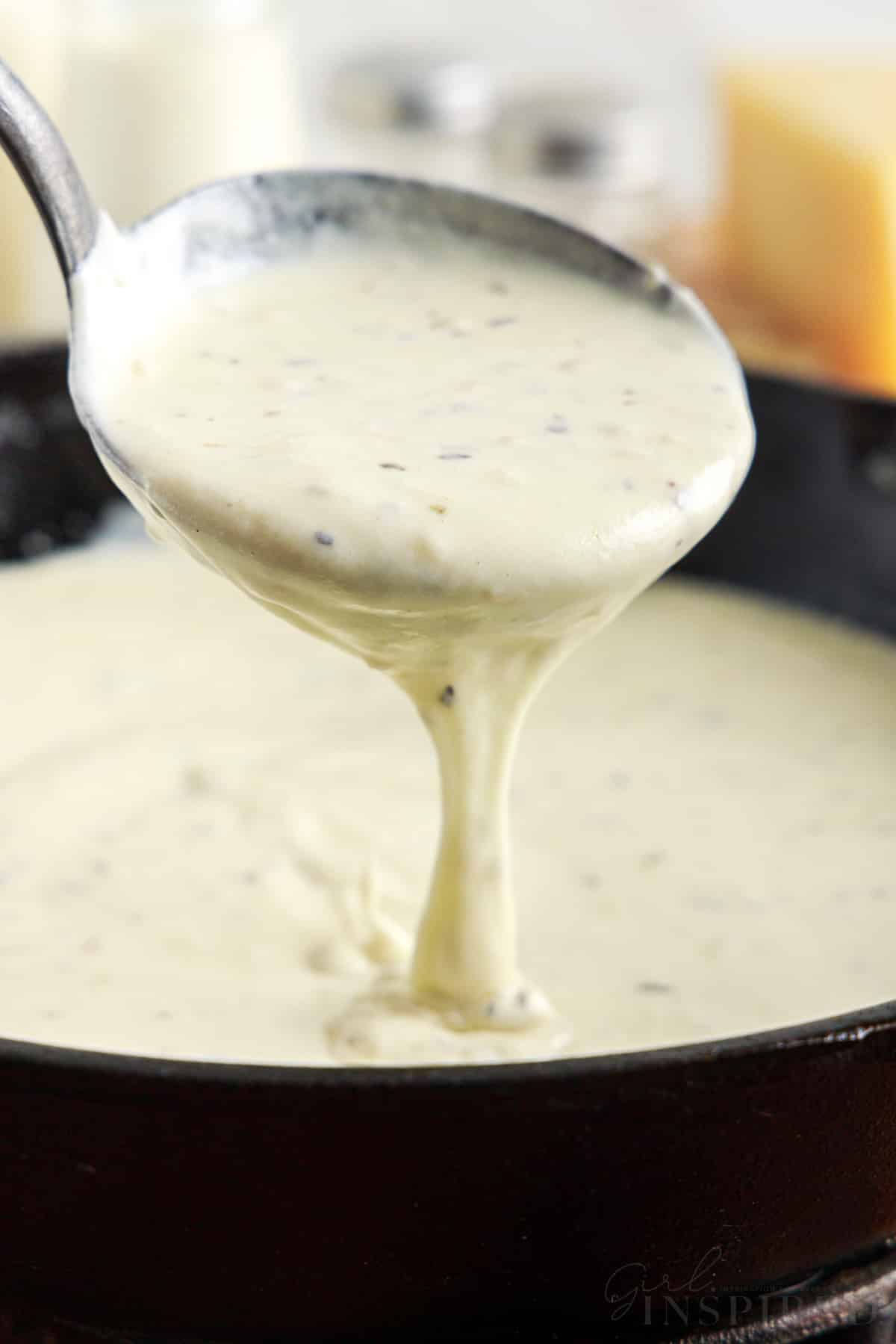 alfredo sauce dripping of ladle into skillet