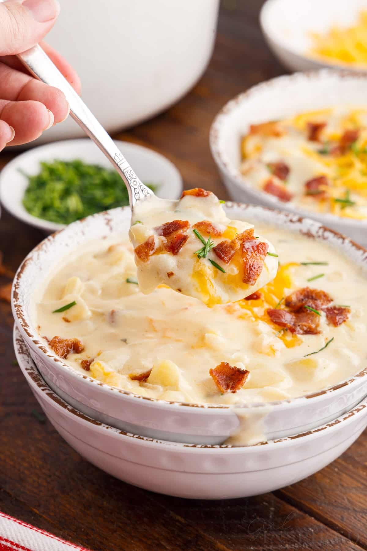 bacon cheddar potato soup in bowls with a spoon lifting soup out