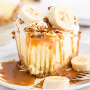 Close-up of banana cream pie with Graham cracker crust on a white serving plate with a forkful of pie removed, metal fork resting on the plate.