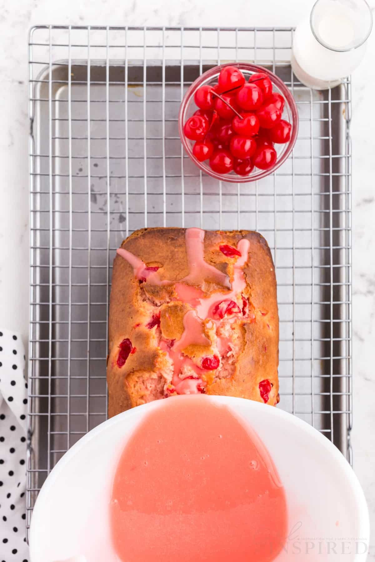 glaze poured on top of cherry bread on wire cooling rack over cookie sheet next to cherries