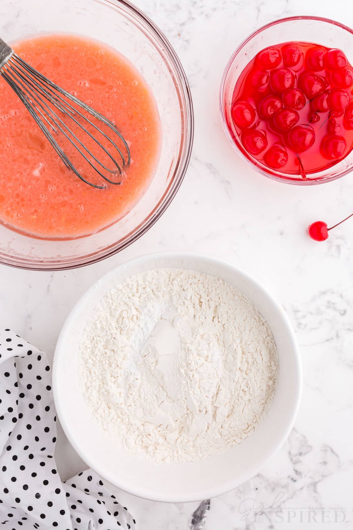 cherry juice mixture with spatula next to bowl of cherries and bowl of flour for cherry bread.