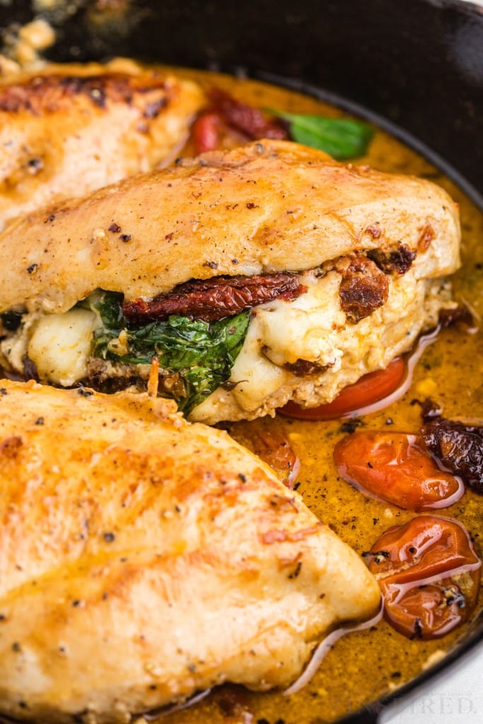 Close up of cooked chicken with sundried tomatoes and spinach in a skillet.