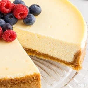 close up of classic cheesecake with berries on top with a slice missing