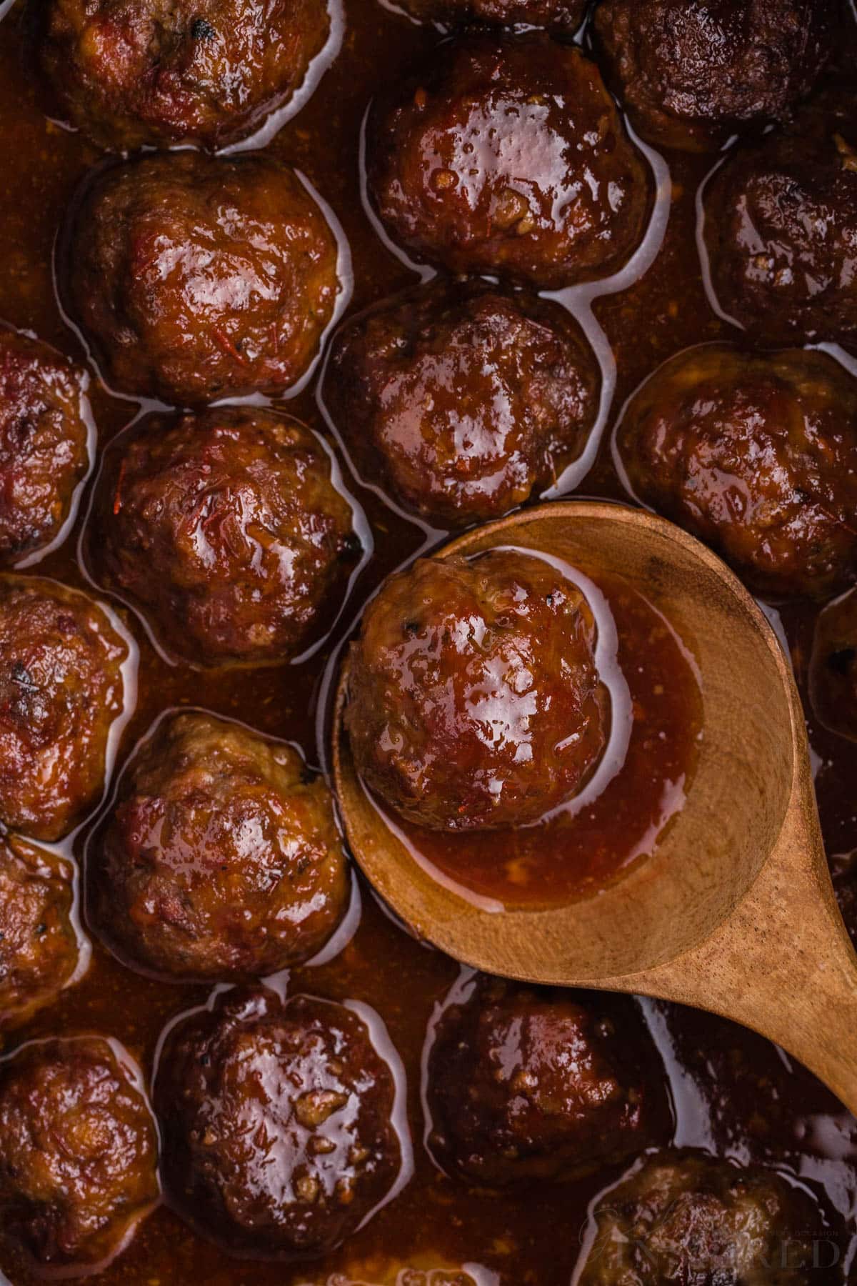 wooden spoon scooping crockpot meatballs with grape jelly and chili sauce