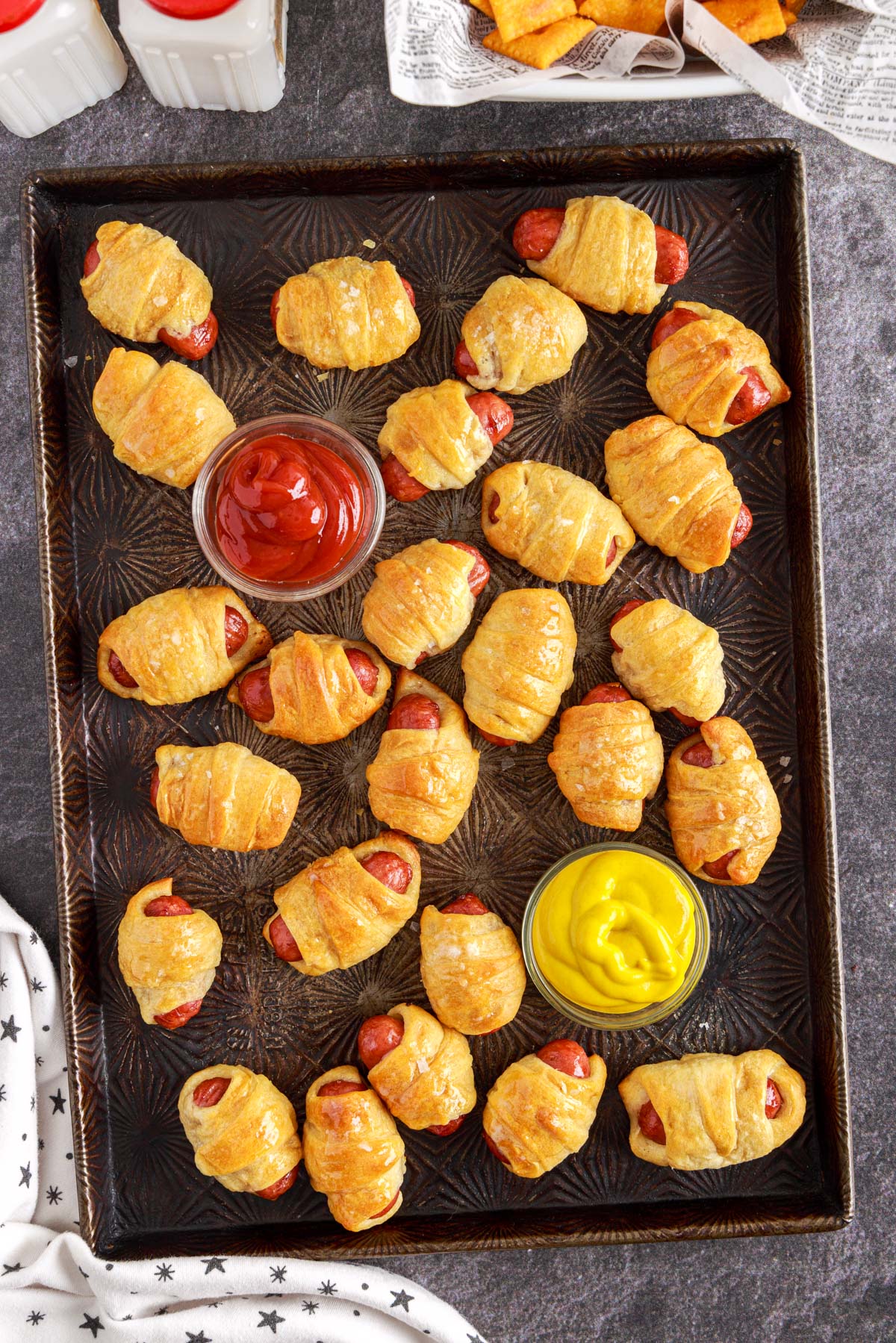 cookie sheet full of lil smokies pigs in a blanket with ketchup and mustard on a cookie sheet