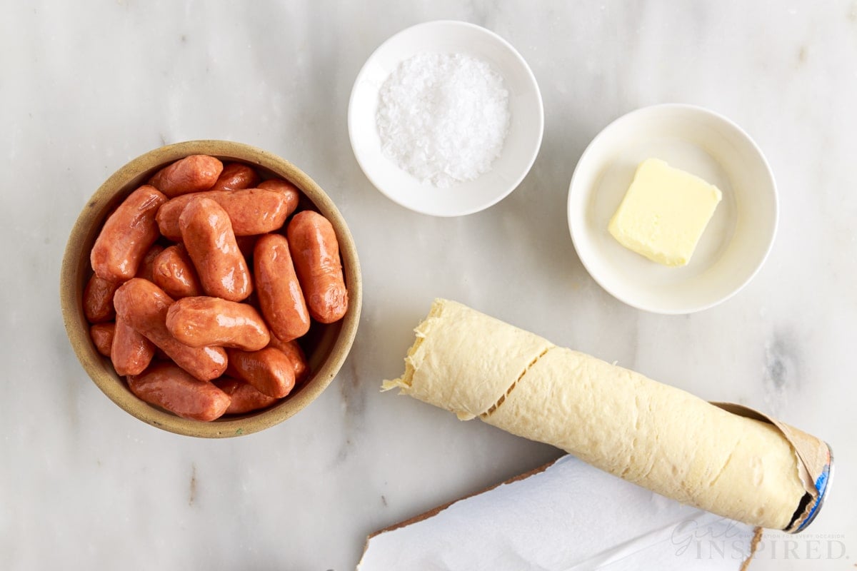 lil smokies in a small dish next to a roll of crescent rolls and a small dish of salt and butter