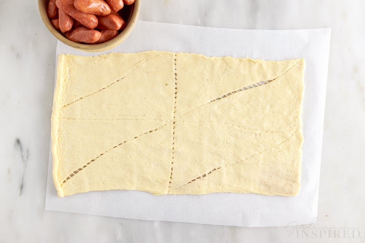 crescent rolls rolled out on parchment paper next to a dish of lil smokies