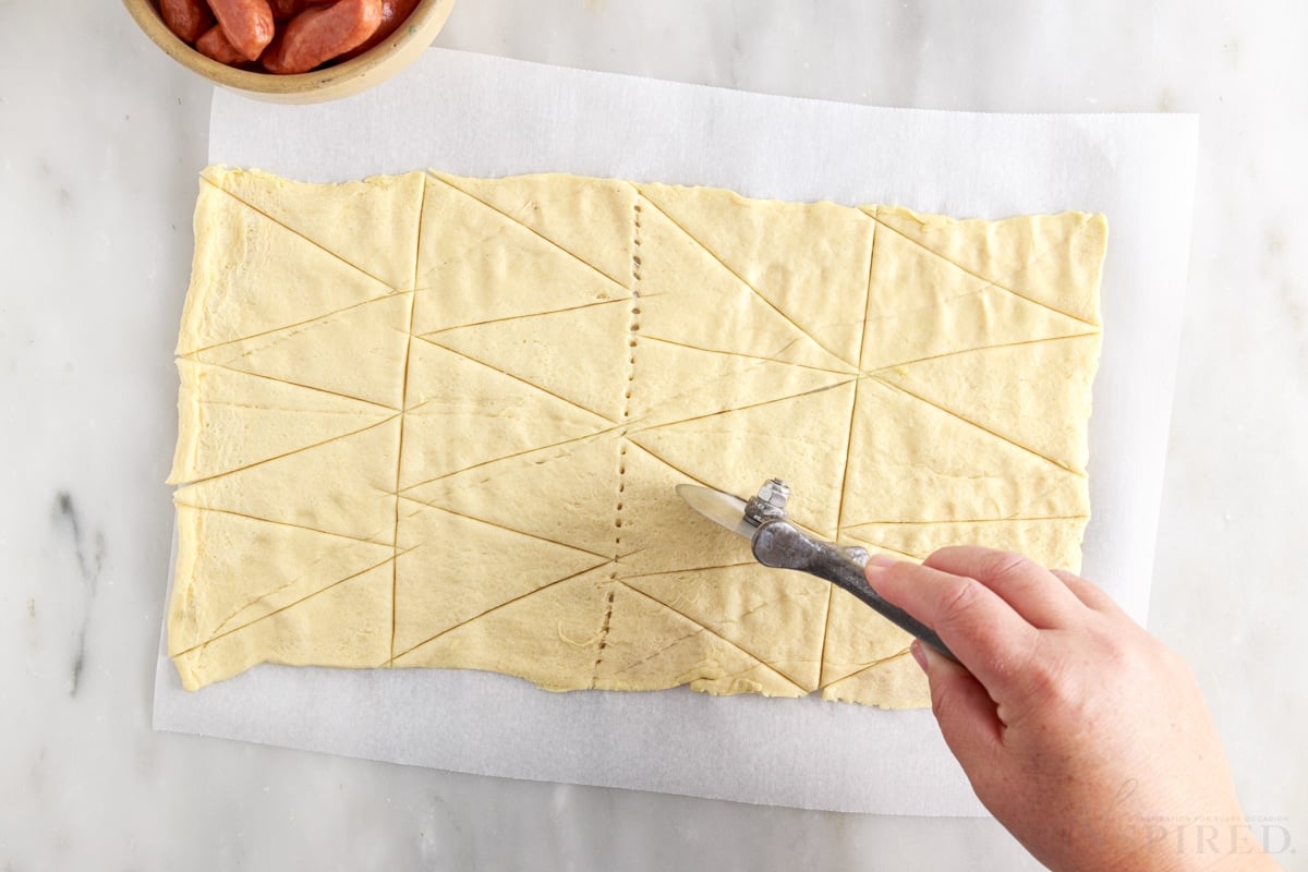 crescent rolls being cut into triangles on parchment paper