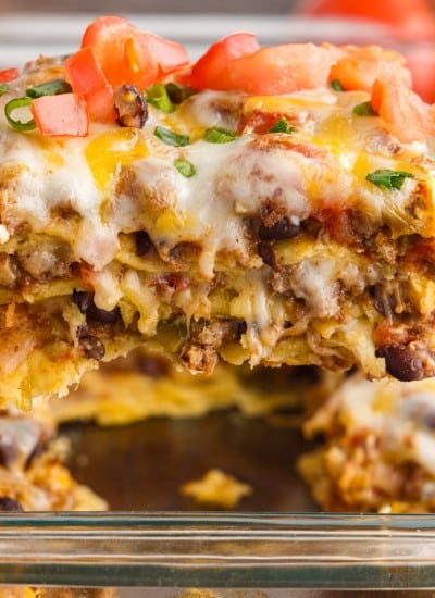slice of mexican lasagna on a spatula over tray of it
