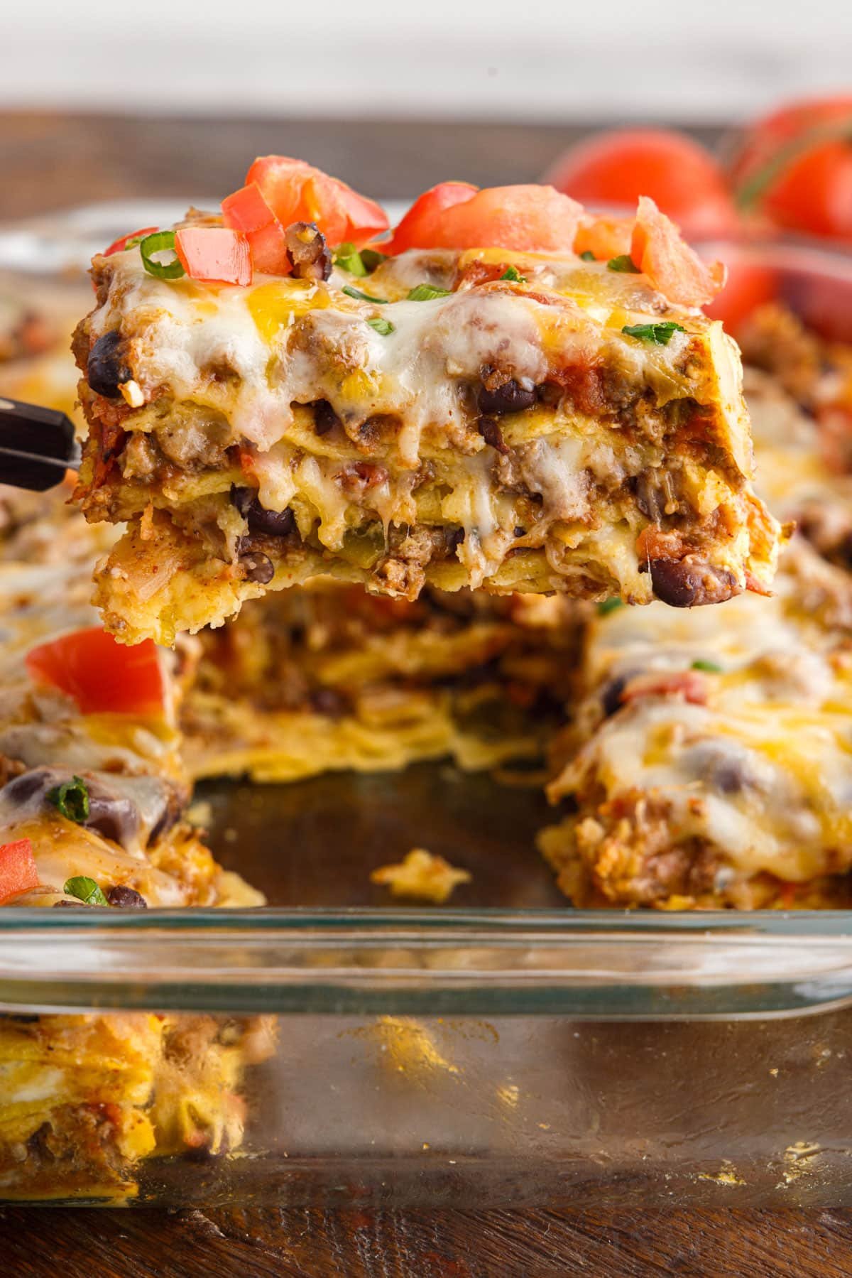 slice of mexican lasagna on a spatula over tray of it