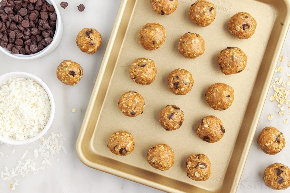 cookie sheet full of balls no bake energy balls next to small dish of coconut and chocolate chips