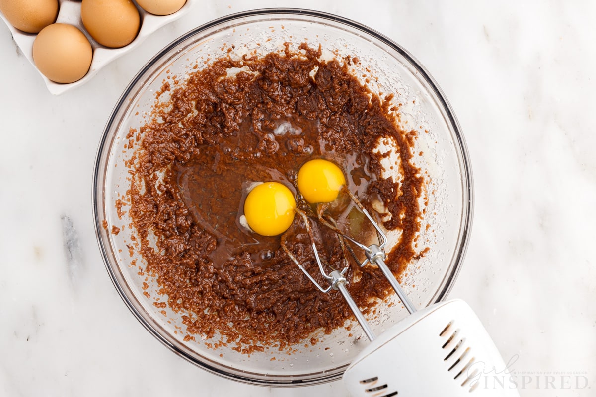 eggs added to chocolate mixture in mixing bowl with mixer next to eggs