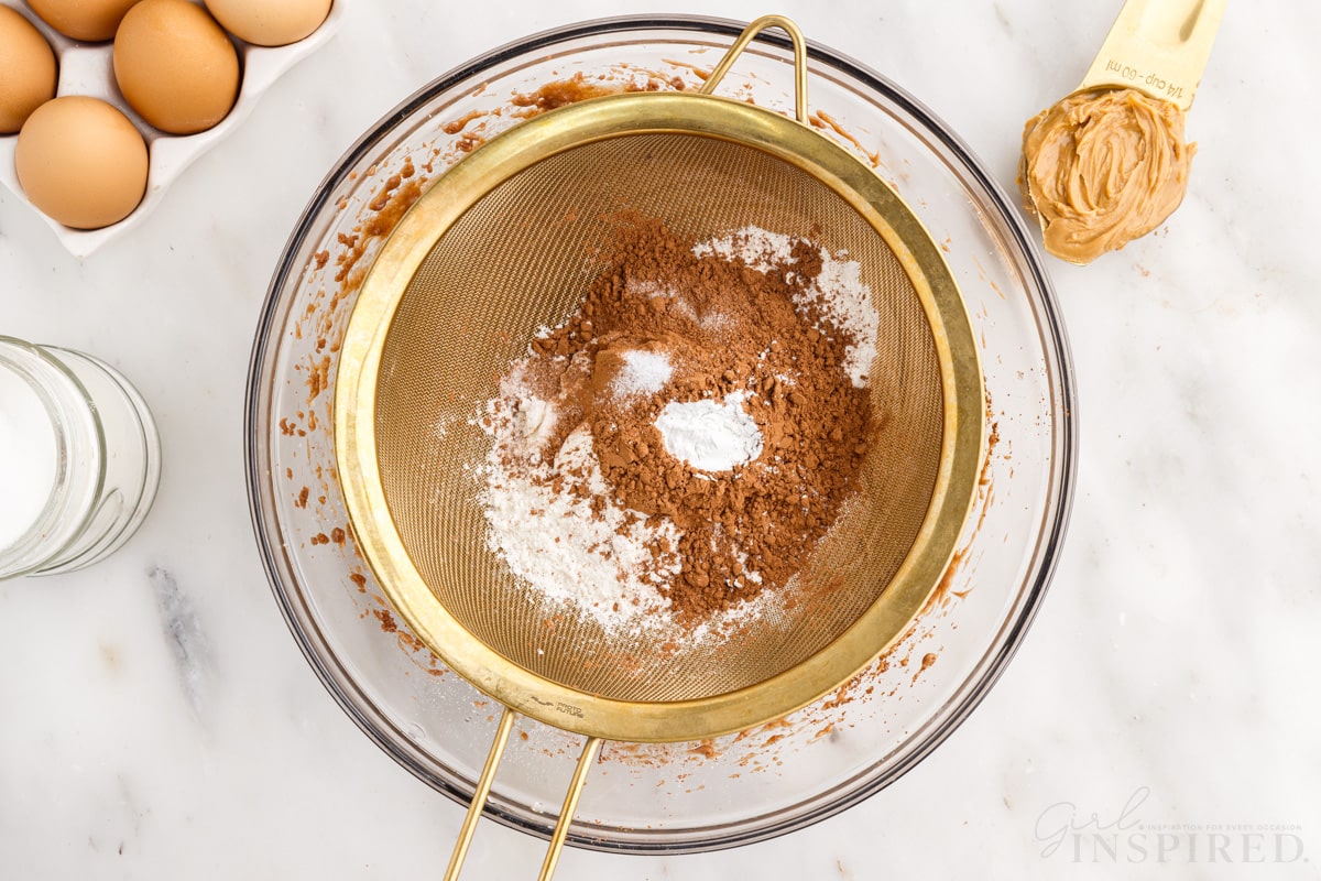 brownie batter, cocoa powder and flour in a sieve over wet ingredients