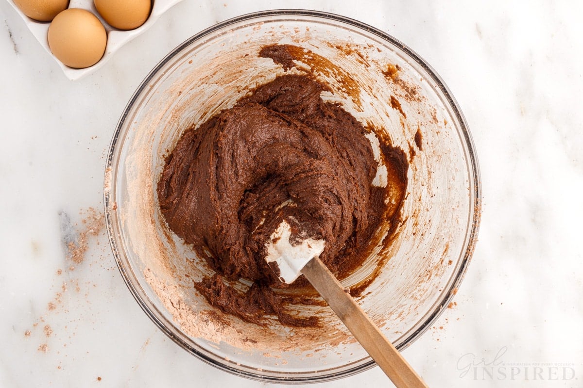 brownie batter mixed together in a mixing bowl with spatula next to eggs