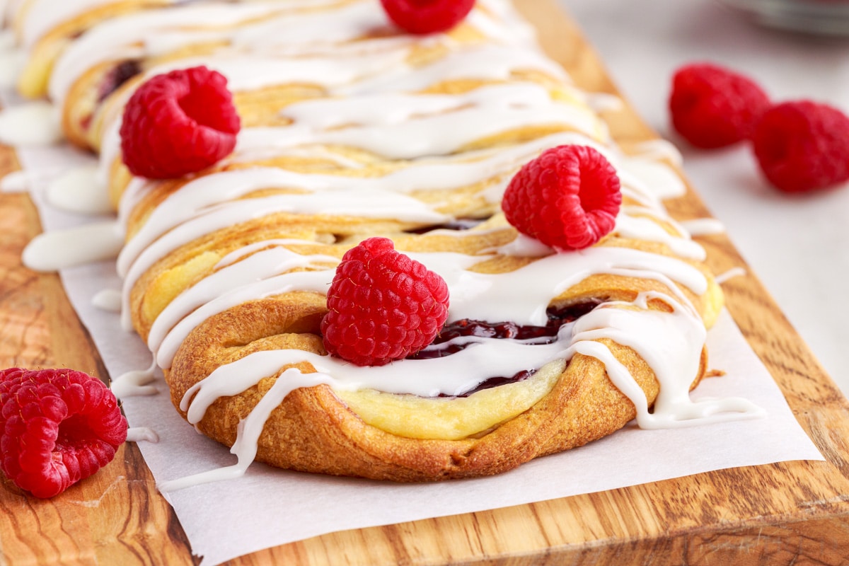 close up of raspberry cream cheese danish with raspberries on a wooden serving board