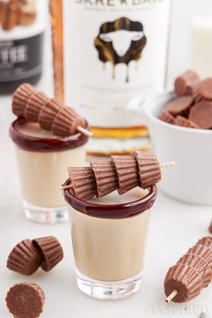 two shot glasses of skrewball whiskey reese cup shots with mini reeses on skewers on top of glasses