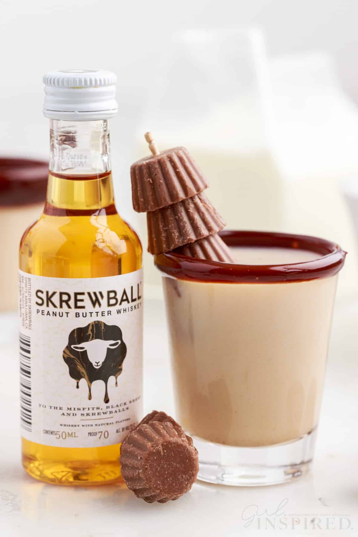 mini bottle of skrewball peanut butter whiskey next to a shot glass of skrewball whiskey reese cup shot with mini peanut butter cups