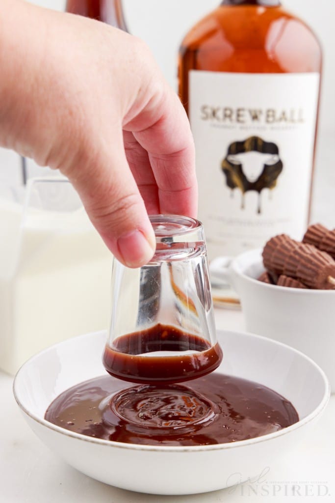 shot glass dipped into chocolate syrup in a small dish and skcrewball whiskey in the background