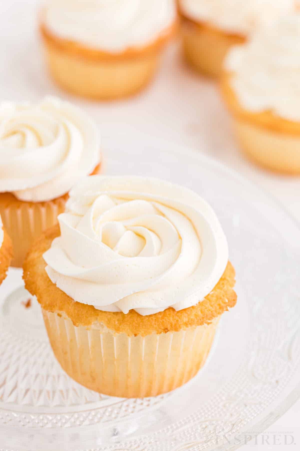 Vanilla cupcakes with swiss meringue buttercream on a glass cake stand.