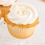 Close-up of vanilla cupcakes with Swiss meringue buttercream on a glass cake stand.
