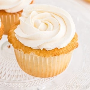 Close-up of vanilla cupcakes with Swiss meringue buttercream on a glass cake stand.