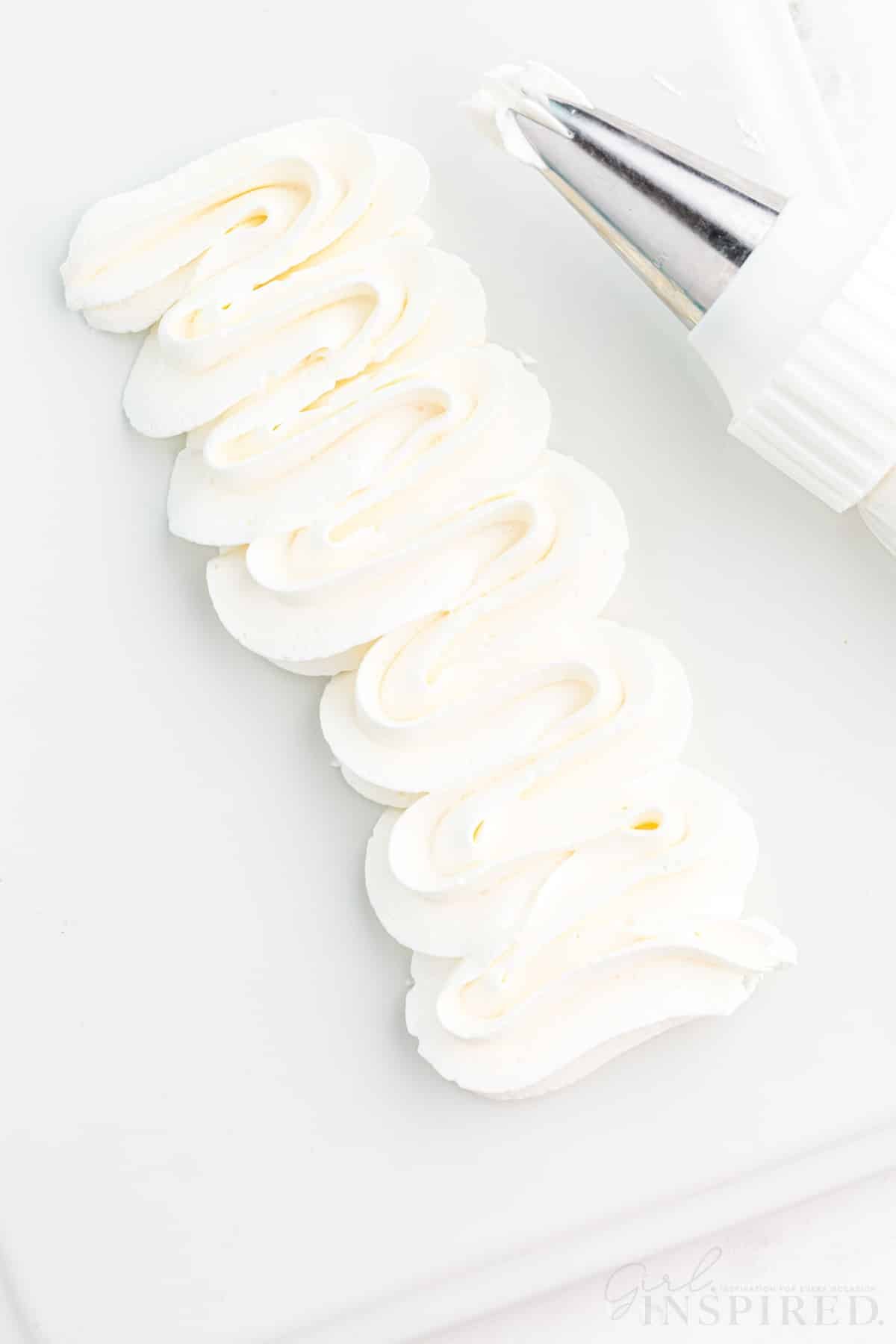 Close-up of piped Swiss meringue buttercream with piping nozzle on a white plastic board, on a marble countertop.