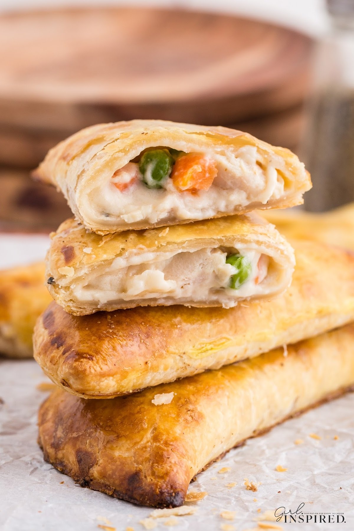 Chicken Pot Pie Hand Pies piled up on top of each other, upper one cut in half, on a wooden kitchen board lined with parchment paper.