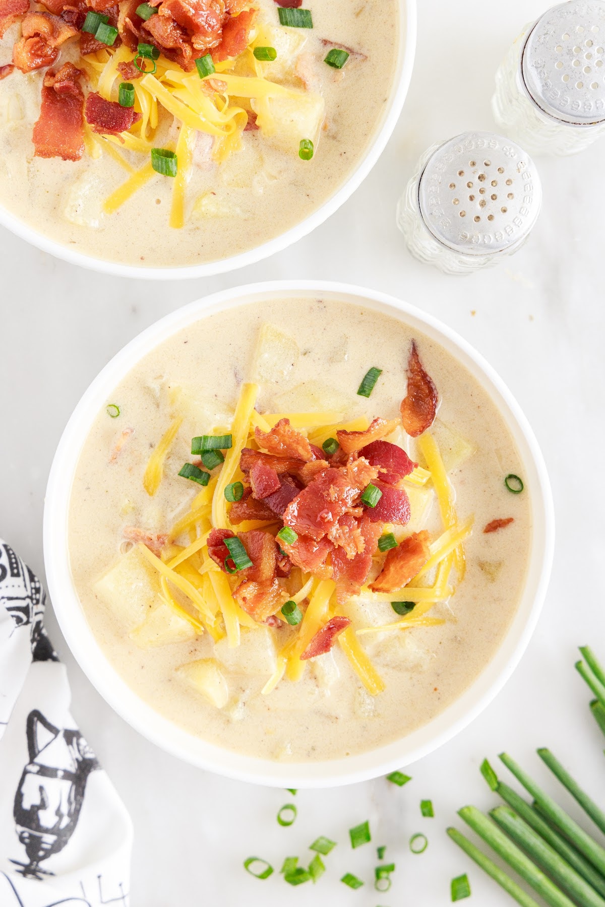 Two bowls filled with loaded baked potato soup, topped with bacon, shredded cheddar, and chives.
