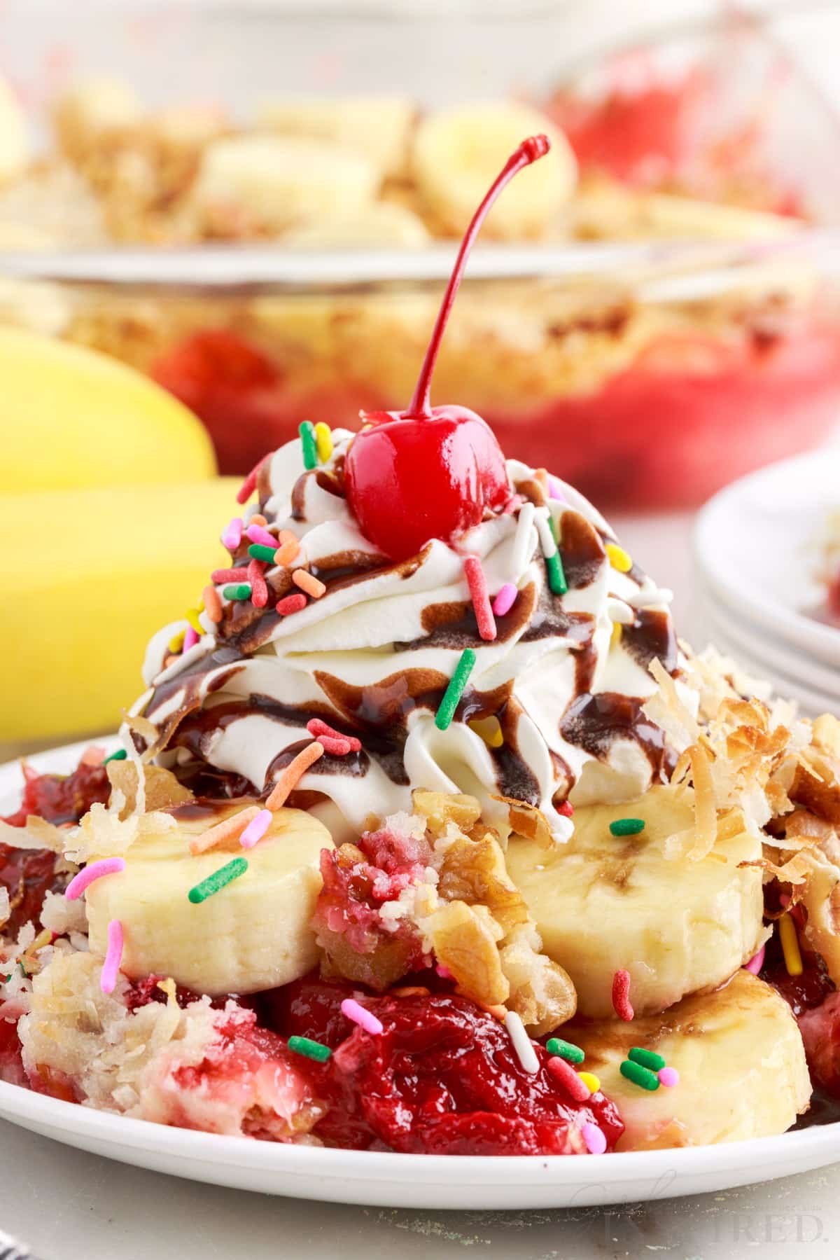 Whipped topping and cherry added to a plate full of banana split dump cake.