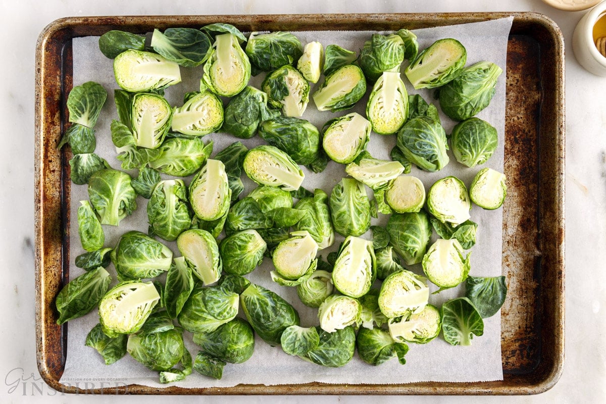 Halved Brussel sprouts spread on a sheet pan lined with parchment paper.