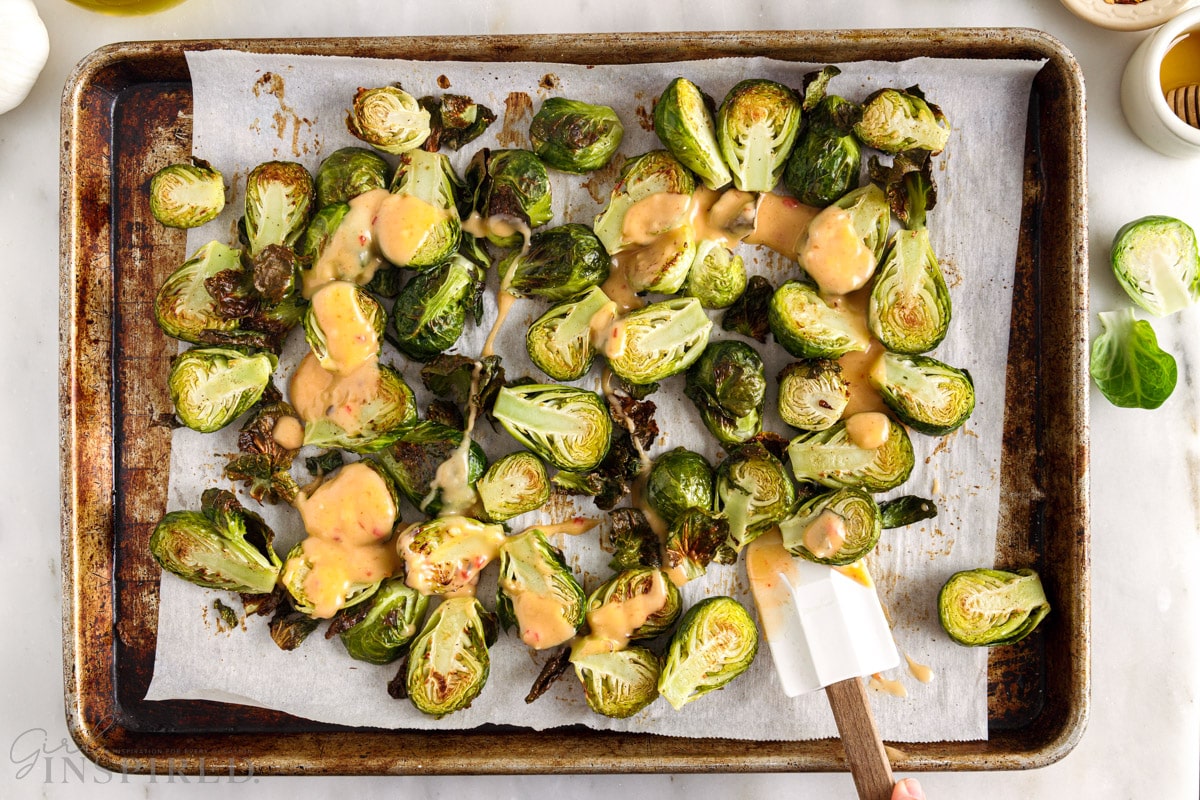Spatula tossing the Bang Bang sauce with the roasted Brussels sprouts.