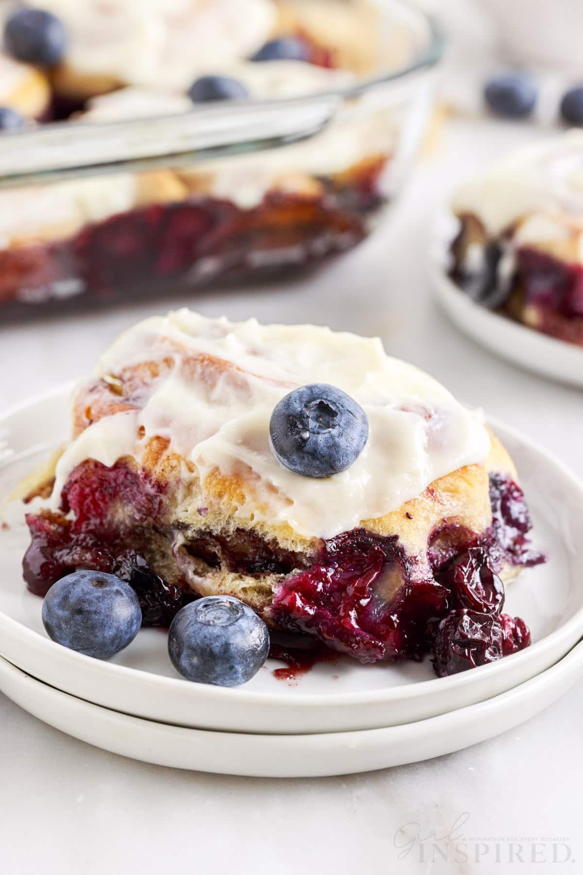 Two stacked plates with a blueberry cinnamon roll on it.