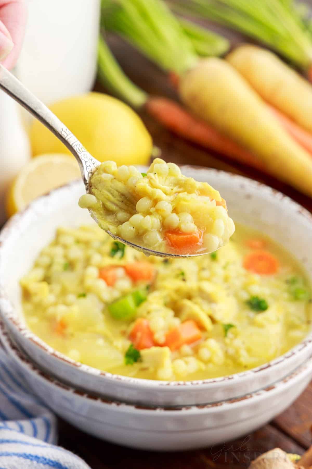 Spoon of chicken couscous soup over bowl of soup.