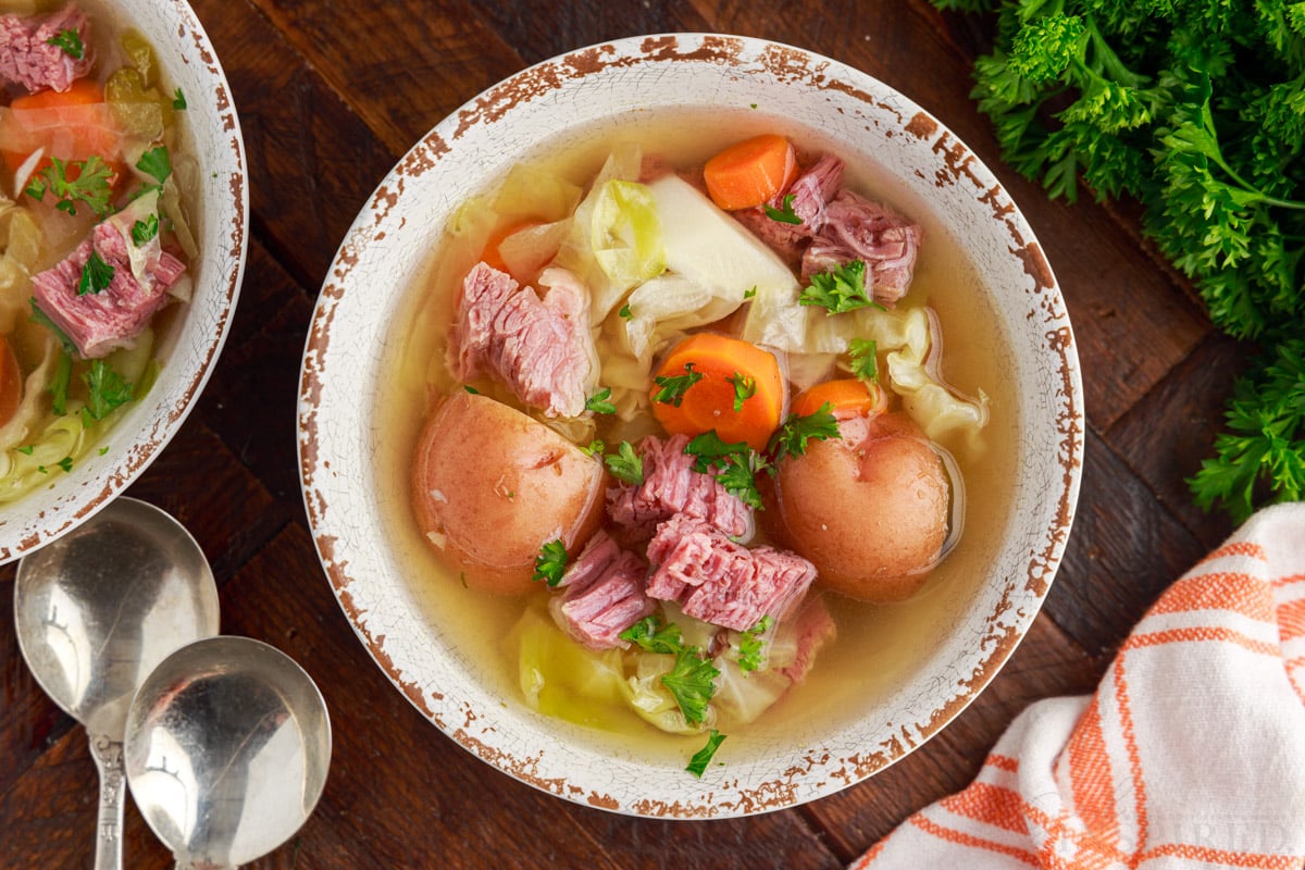 corned beef and cabbage soup in a bowl next to soup spoons