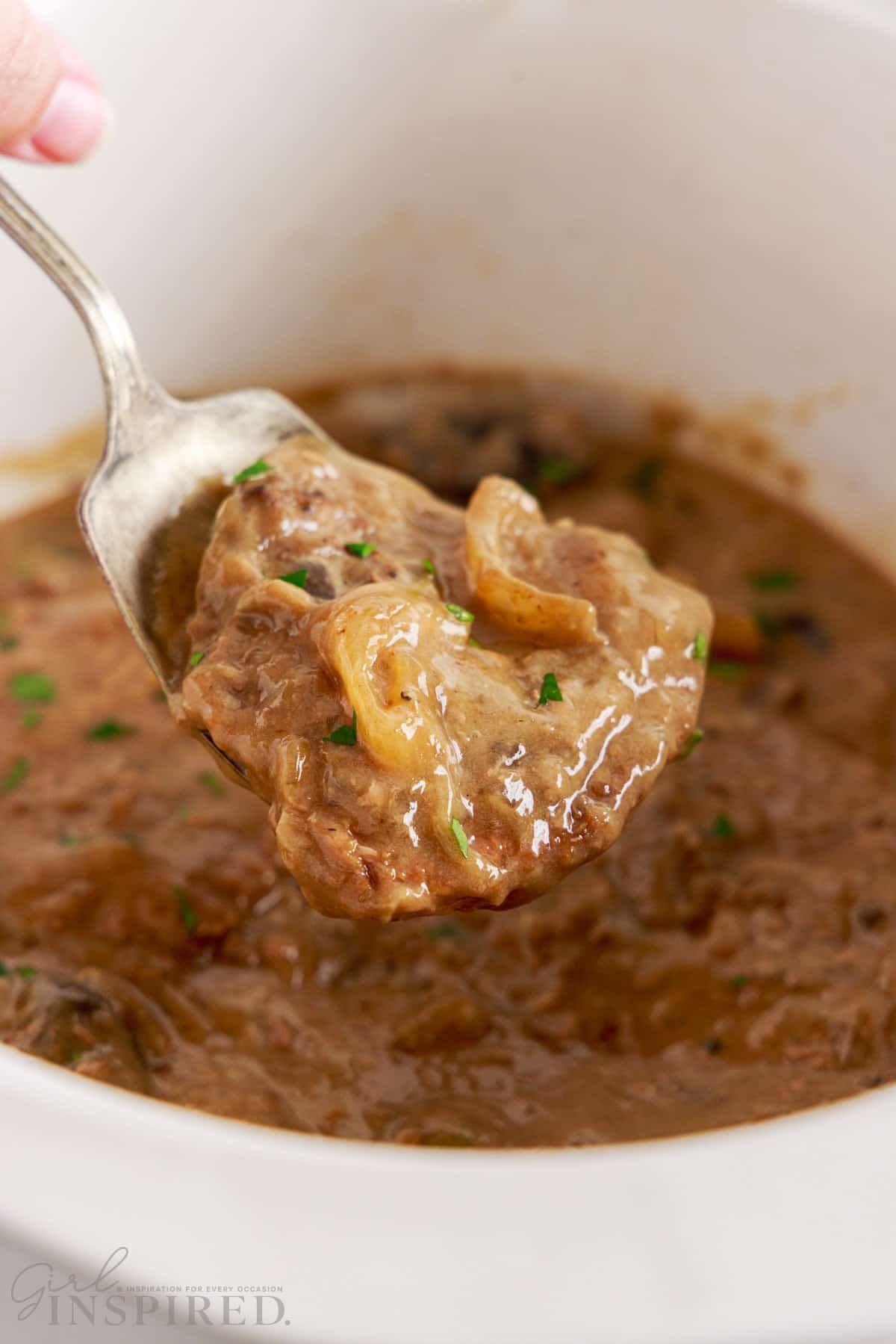 Serving spoon filled with crock pot cube steak lifted from crock.