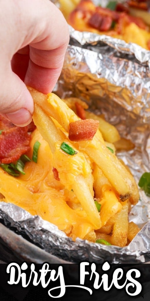 A hand picking up dirty fries from a foil boat baked in baking sheet.