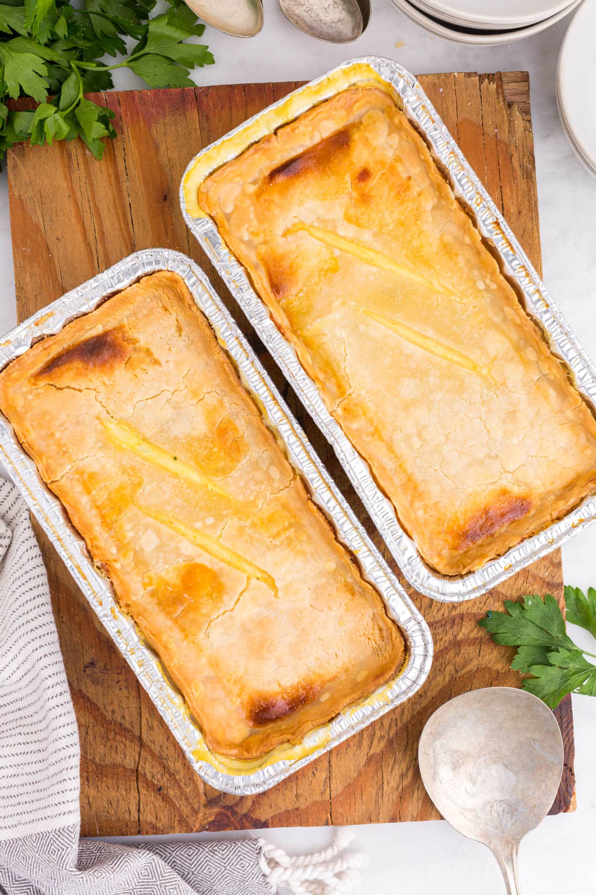 Overhead view of two baked Freezer Chicken Pot Pies resting on a wooden kitchen board.