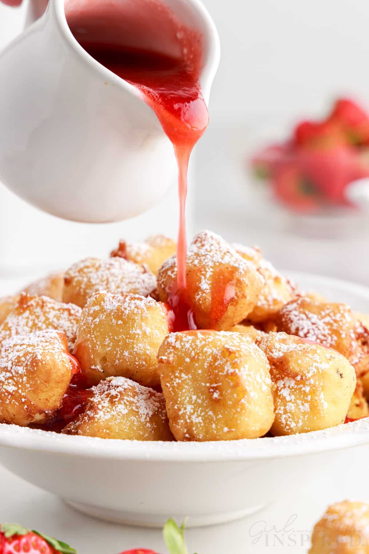 Strawberry sauce being drizzled on top of fried cheesecakes.