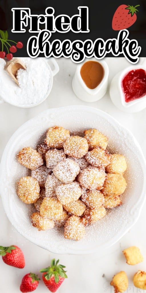 Decorative raised plate full of fried cheesecake with strawberries, caramel sauce, strawberry sauce and powdered sugar around it on a marble countertop