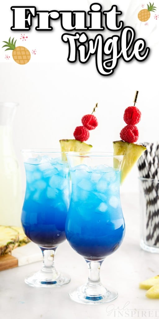 Two tall glasses with fruit tingle cocktail and garnished with pineapple wedges and skewered raspberries, glass jar filled with striped straws, wooden kitchen board with sliced pineapple, jug of lemonade, pineapple garnish on a marble countertop.