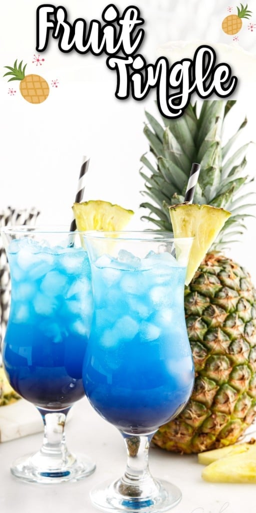 Two tall glasses with fruit tingle cocktail, whole pineapple positioned upright, glass jar filled with striped drinking straws, pineapple wedge garnish on a marble countertop.