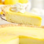 Close up of a slice of lemon custard pie on a server with whipped cream.