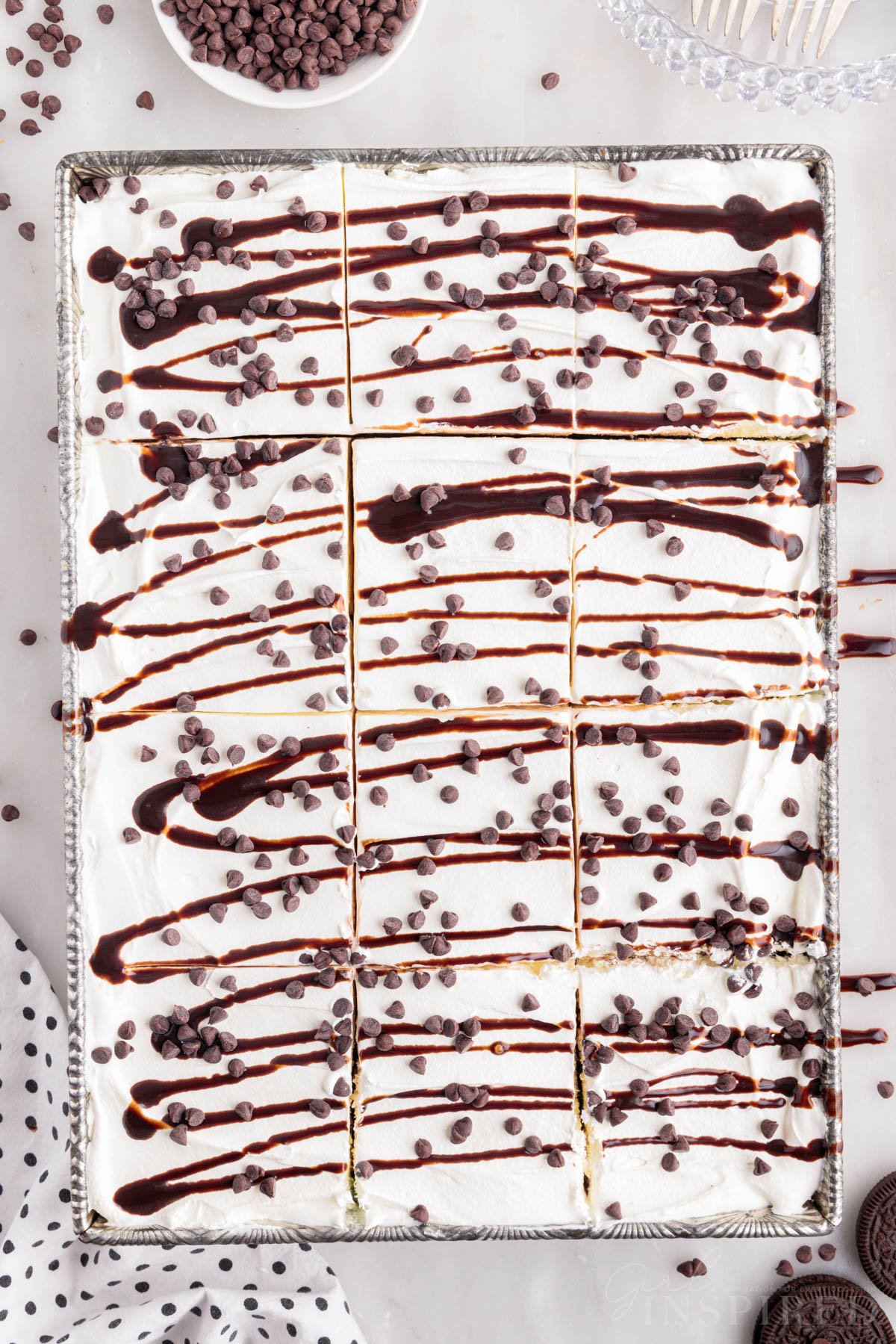 Mint chocolate chip ice cream cake cut into slices with hot fudge drizzle and mini chocolate chips in 9x13 pan.