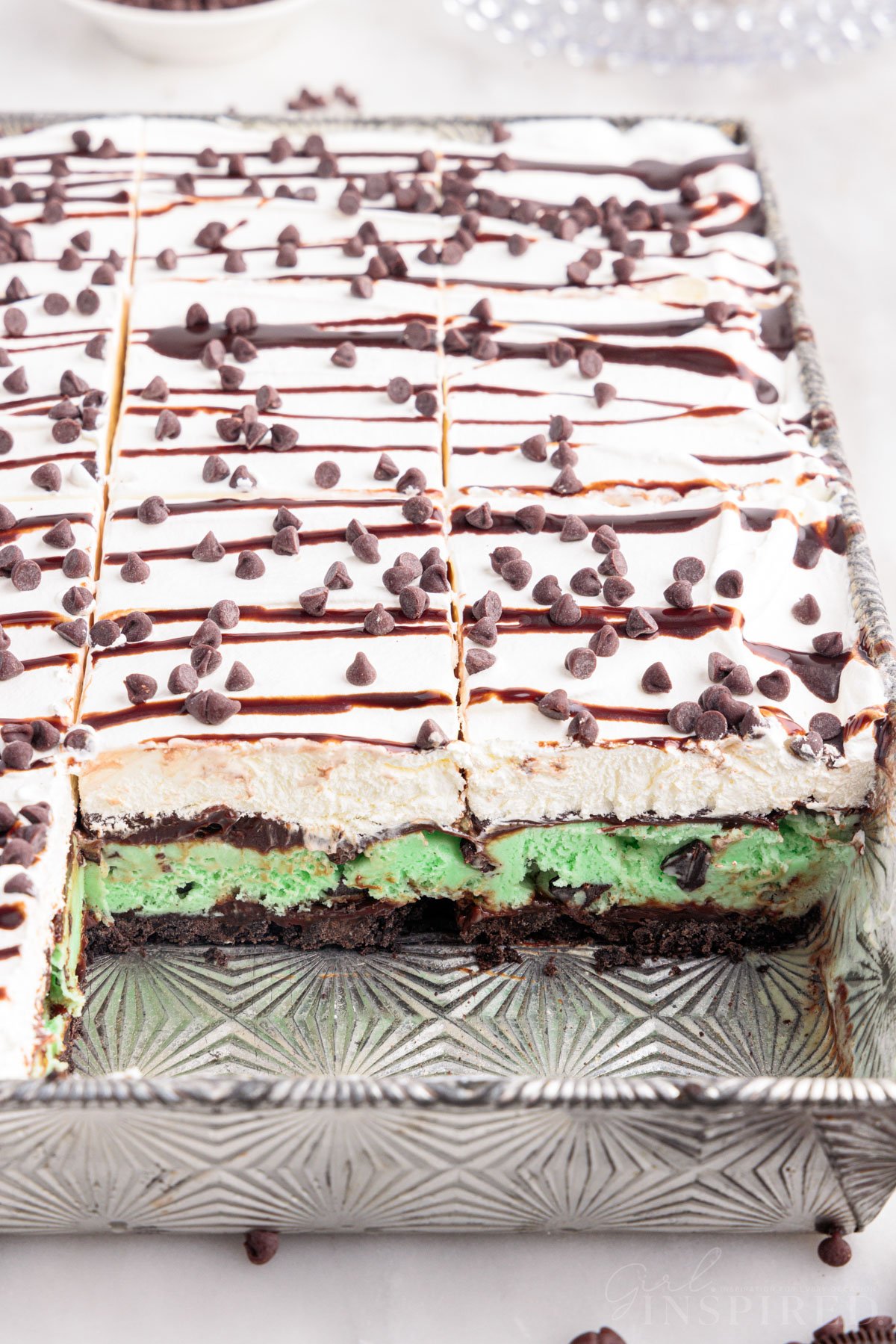Mint ice cream cake in metal pan with several slices removed revealing the layered dessert.
