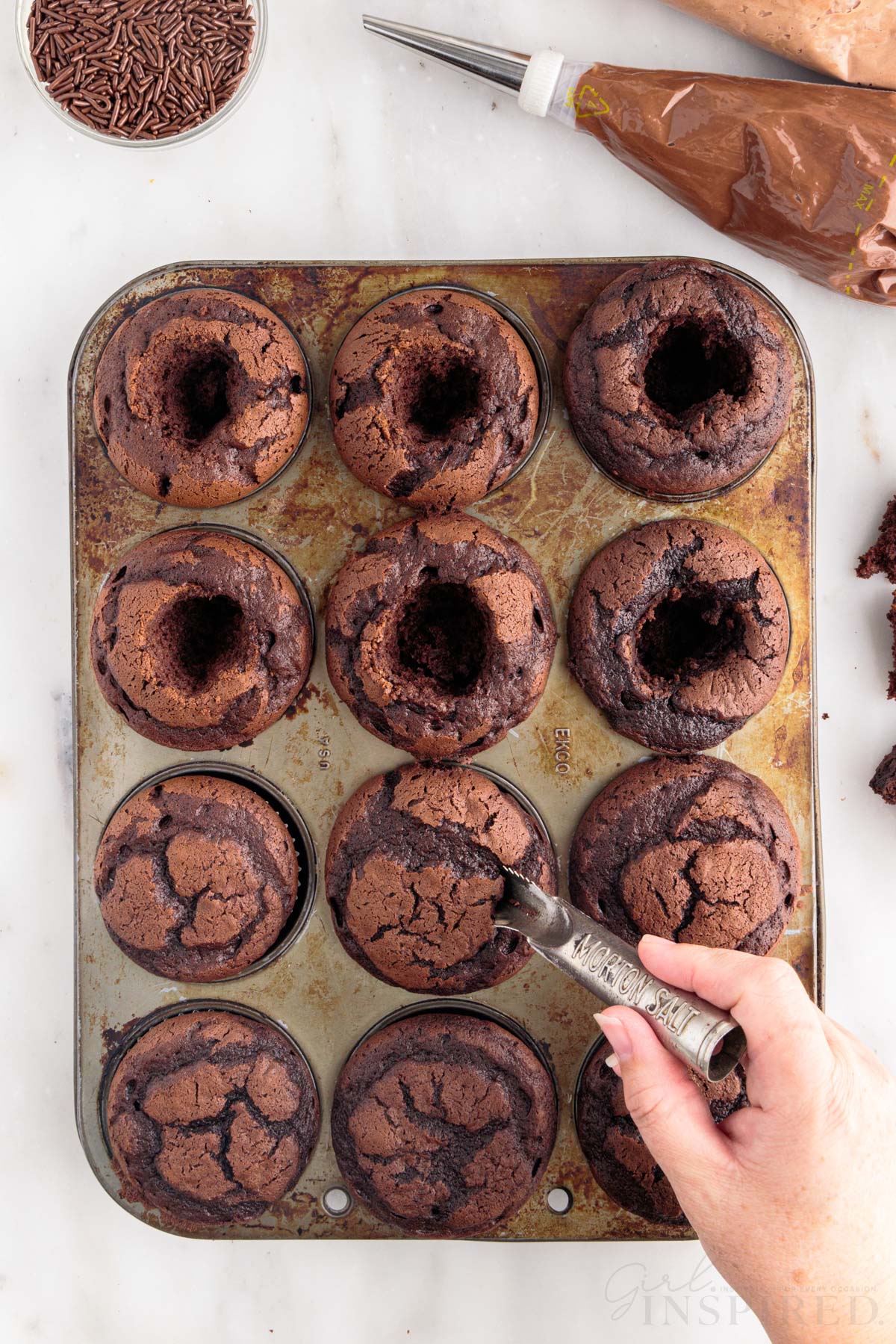 Small holes being carved out of Nutella Cupcakes in muffin tins.