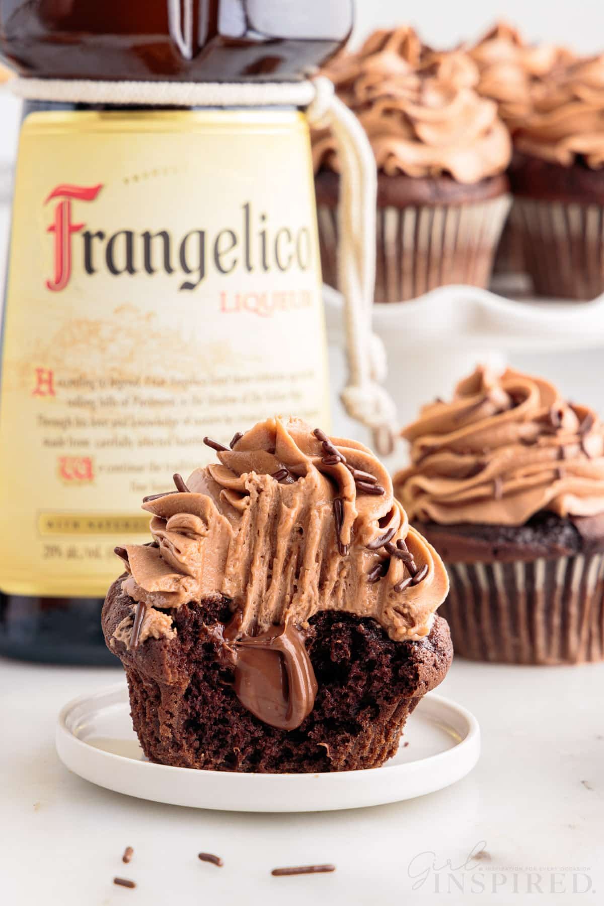 Nutella Cupcakes with a bottle of Frangelico in the background, a bite taken from the front cupcake.