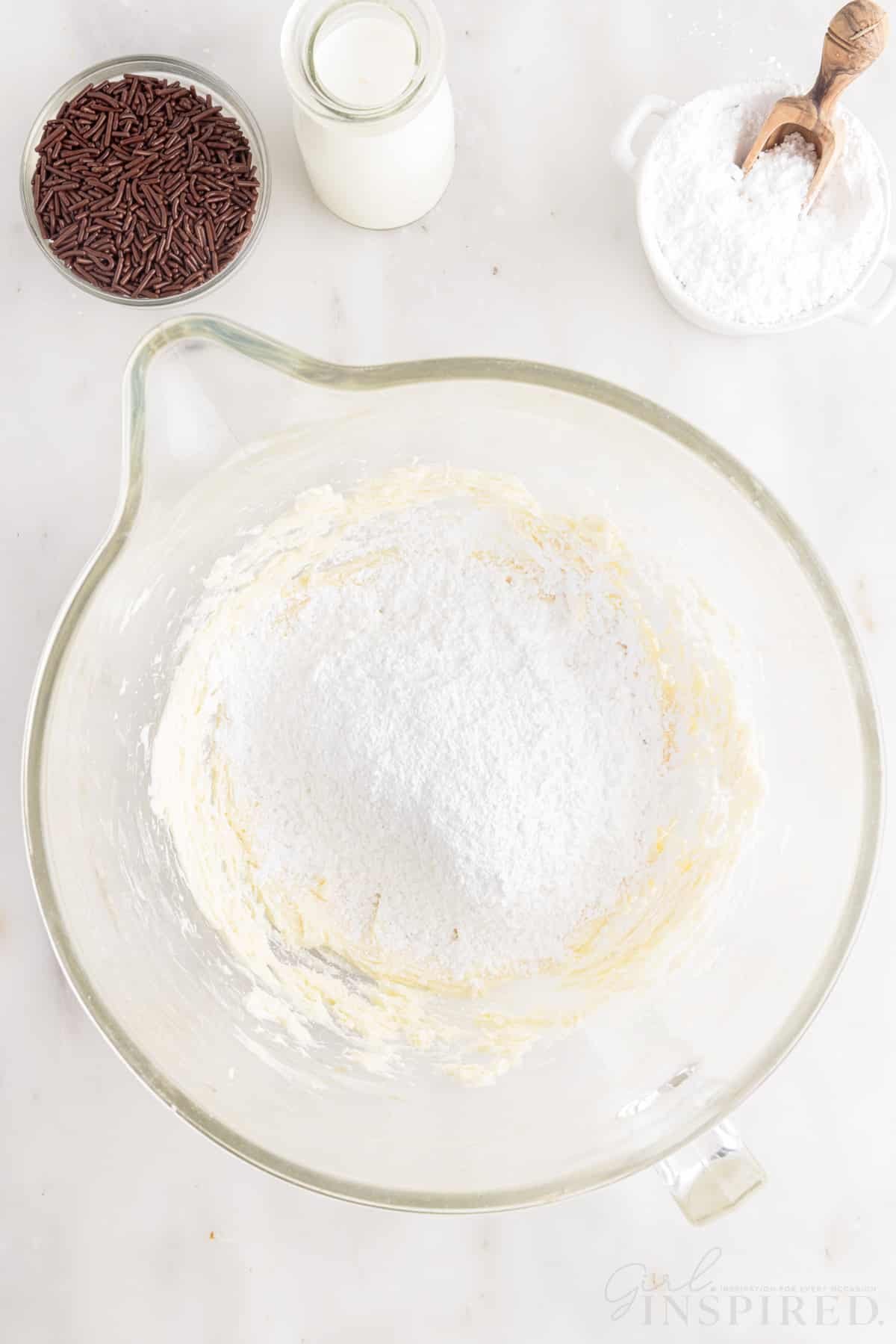 Powdered sugar added to frosting in a mixing bowl.