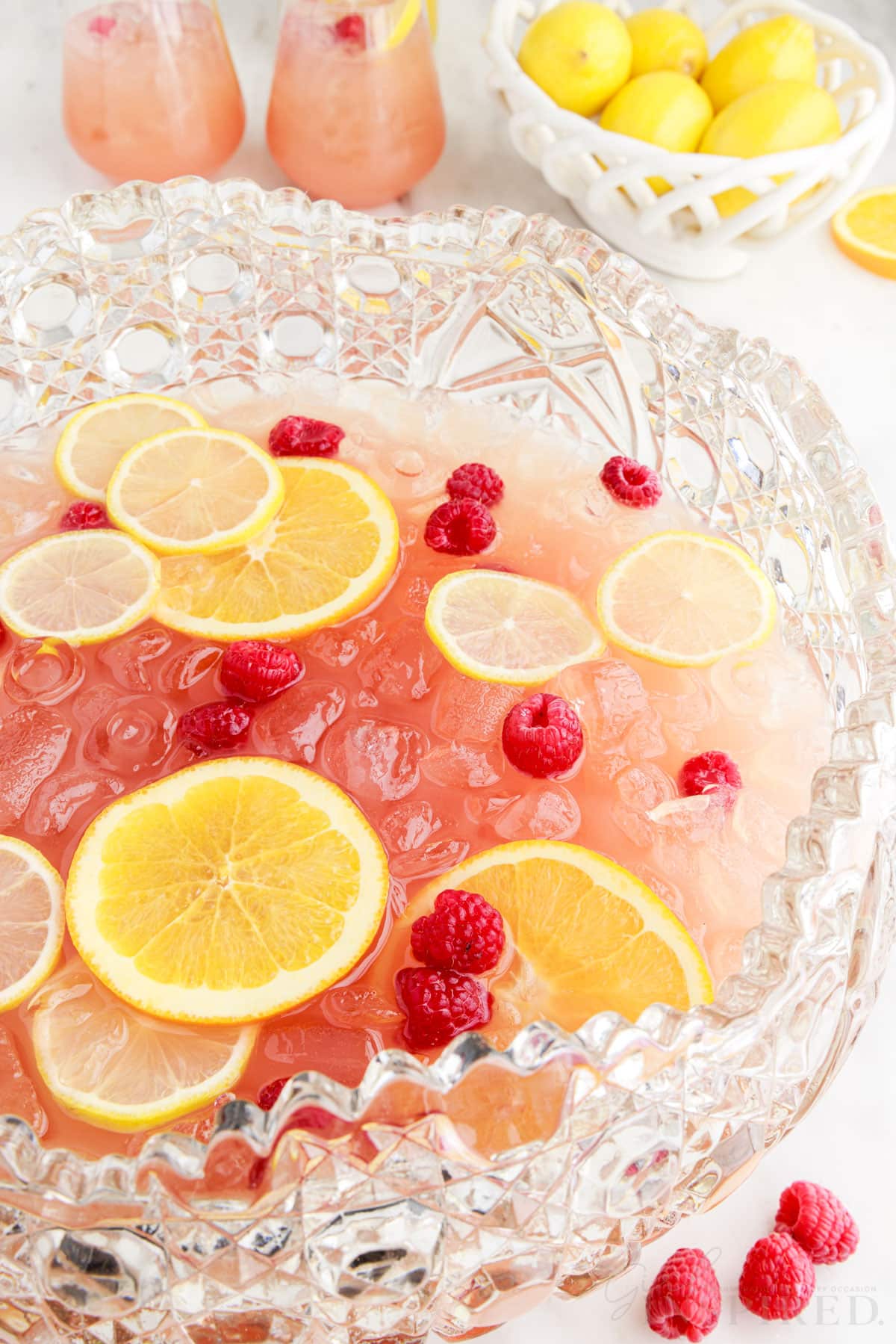 Lemon and orange slices, and fresh raspberries, floating on top of party punch recipe in punch bowl.