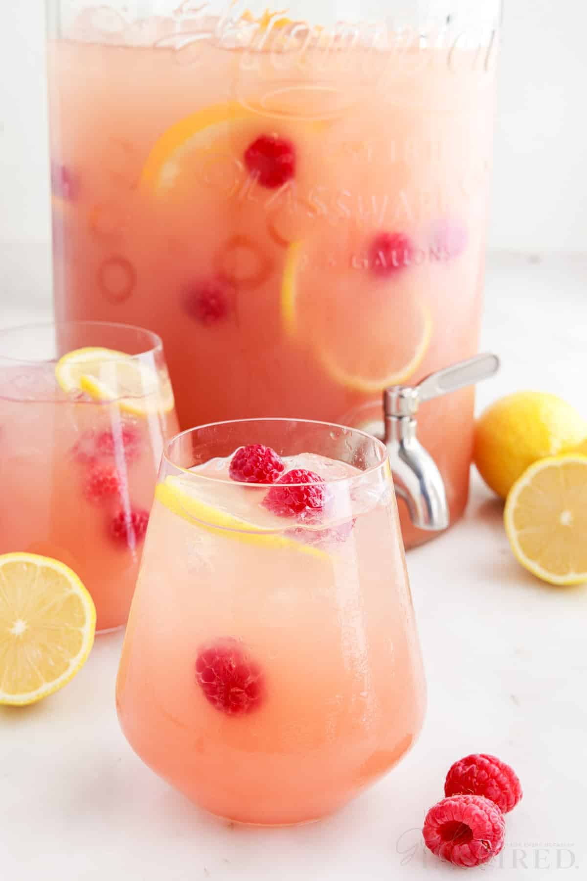 Glasses filled with party punch in front of a large glass beverage dispenser.