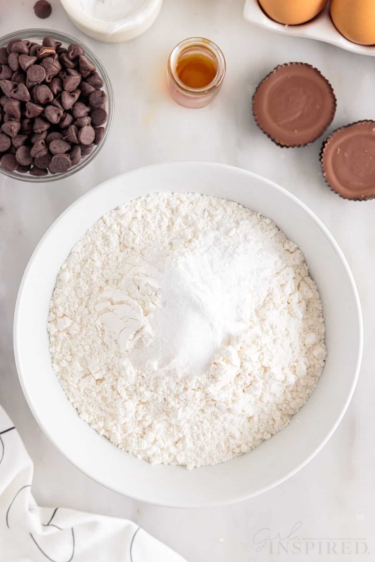 Flour, baking soda, and salt in mixing bowl next to chocolate chips and peanut butter cups.